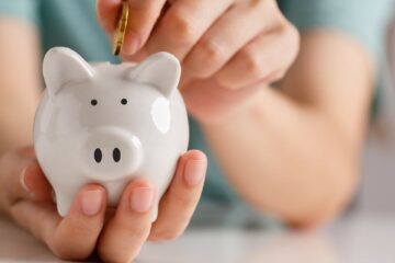 Close-up of hands putting a coin into a piggy bank.