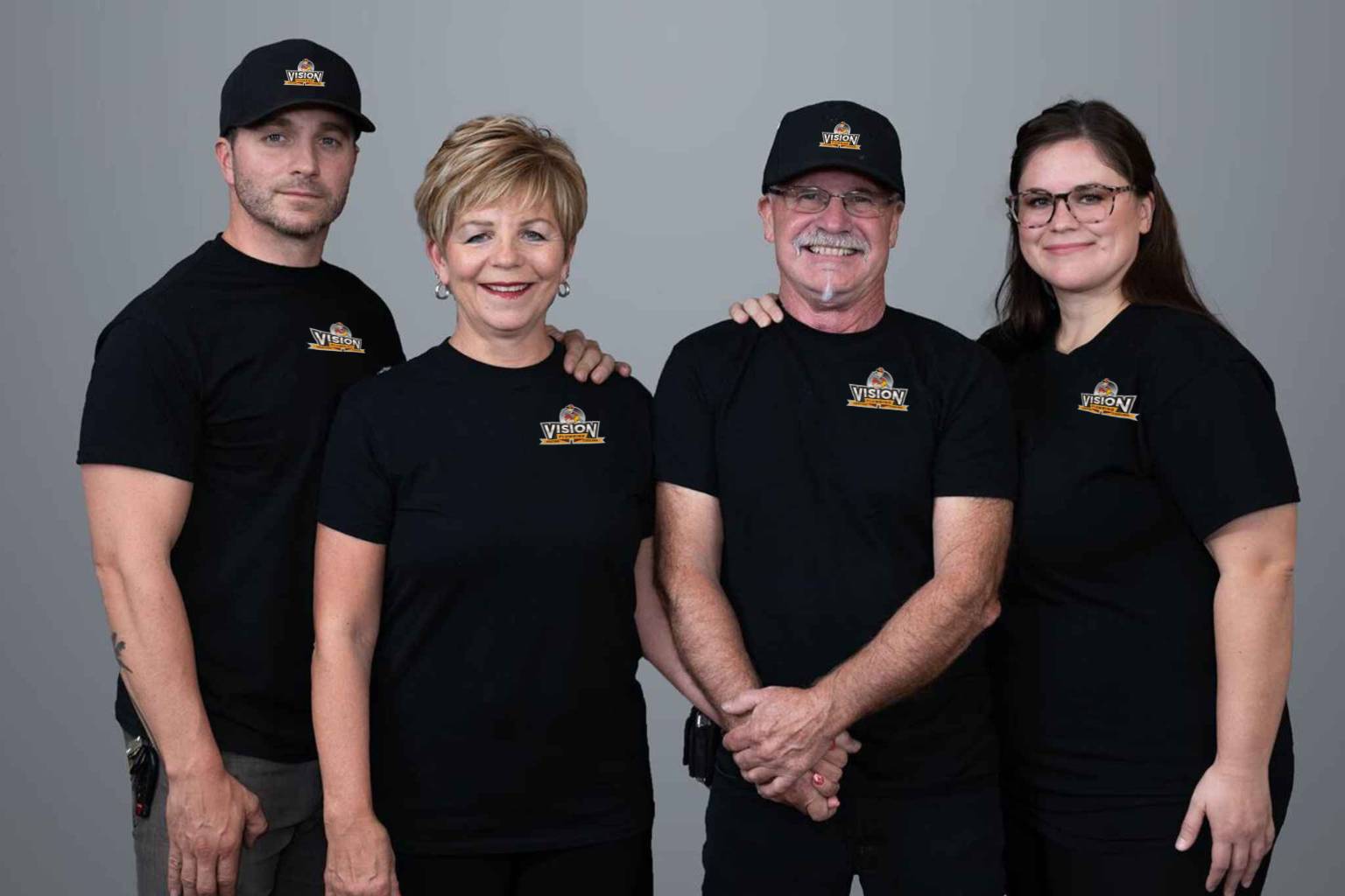 Vision Plumbing Heating Cooling's management team standing side-by-side wearing black t-shirts and hats with their new logo.