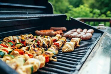 A gas barbeque with meat and vegetable skewers on it
