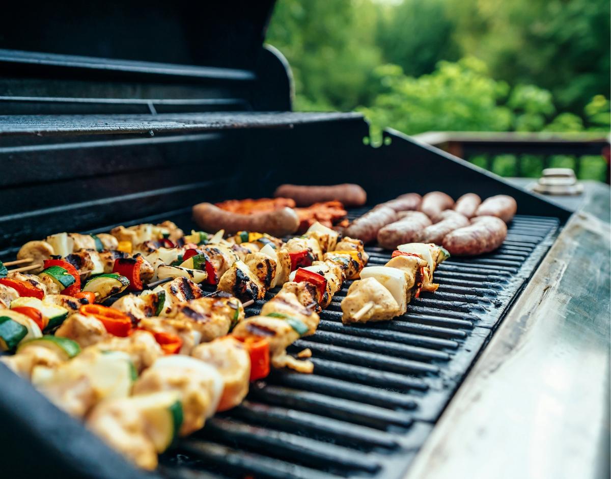 A gas barbeque with meat and vegetable skewers on it