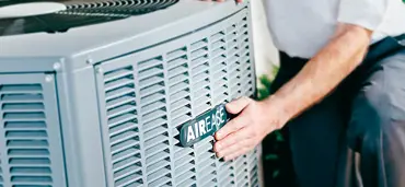 Close-up of an AirEase central air conditioner with a person's hand on the AirEase logo.